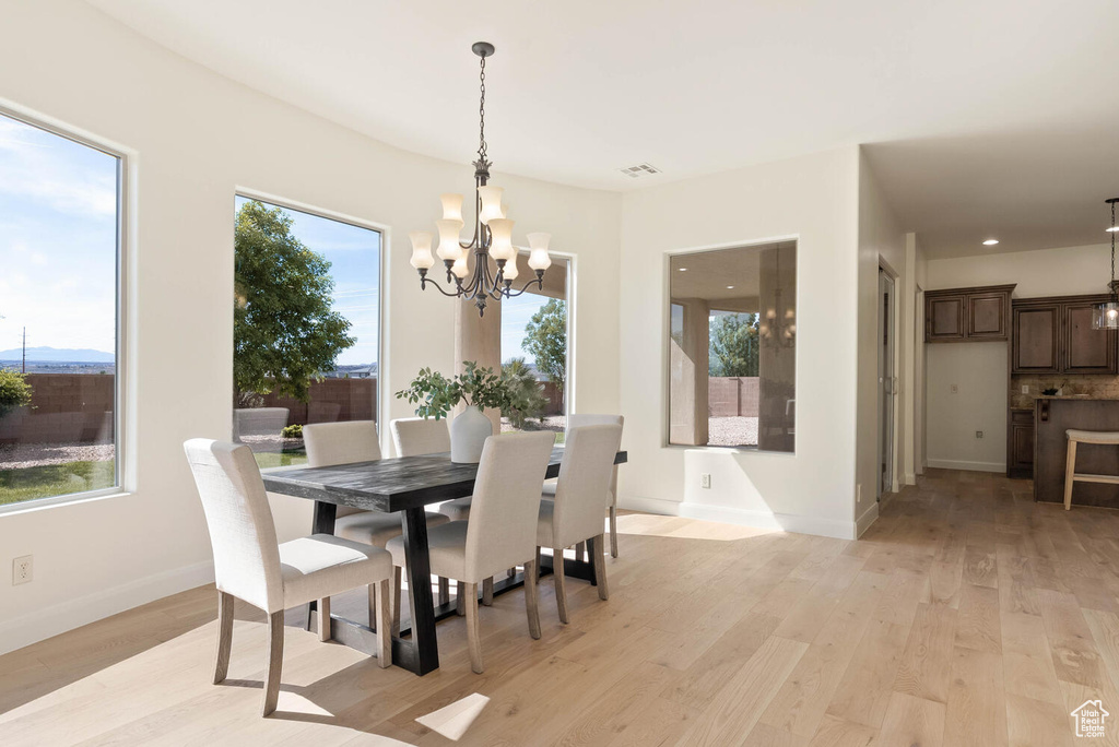 Dining area with a chandelier, light wood-style floors, and healthy amount of natural light