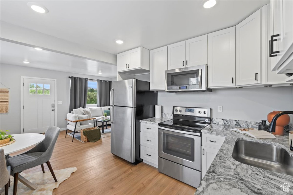 Kitchen with appliances with stainless steel finishes, a sink, white cabinets, light wood-style floors, and recessed lighting