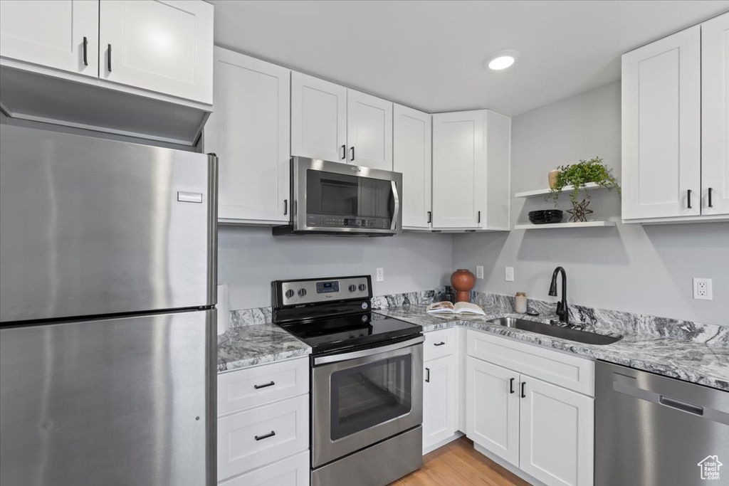 Kitchen with stainless steel appliances, a sink, light stone countertops, and white cabinetry