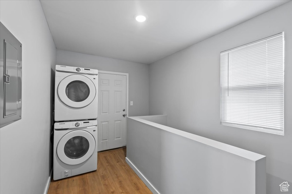 Laundry room featuring stacked washer and clothes dryer, wood finished floors, and baseboards
