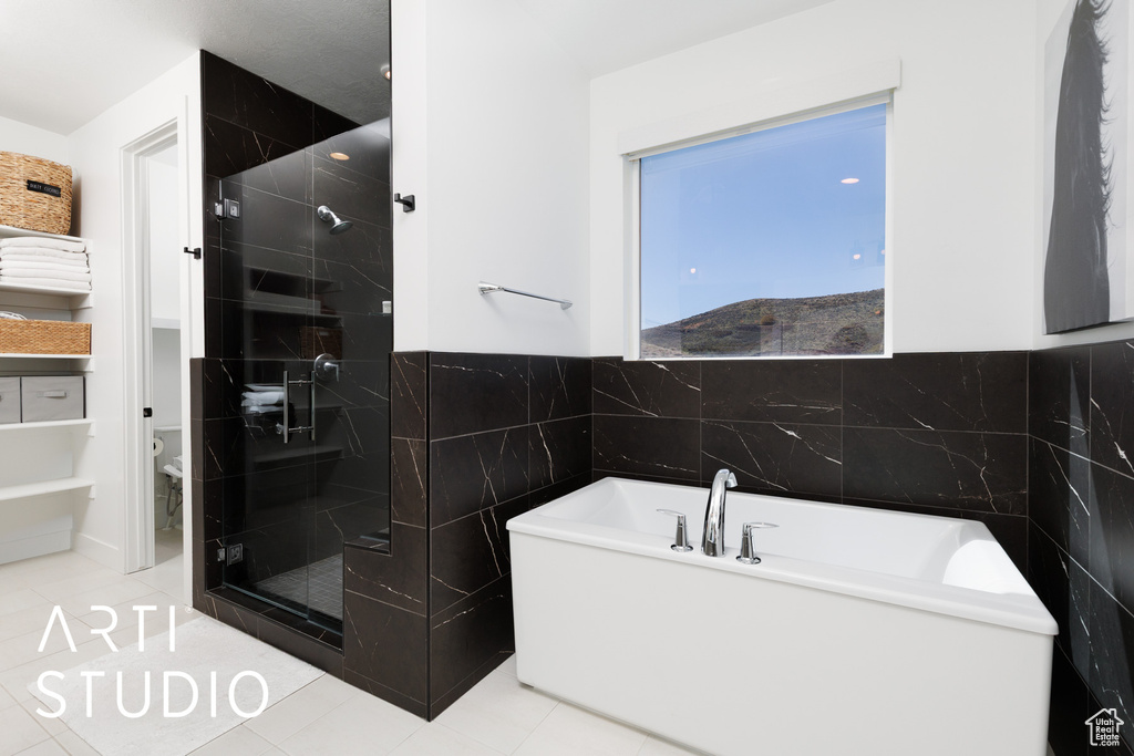 Bathroom featuring tile patterned flooring, toilet, tile walls, a freestanding bath, and a shower stall