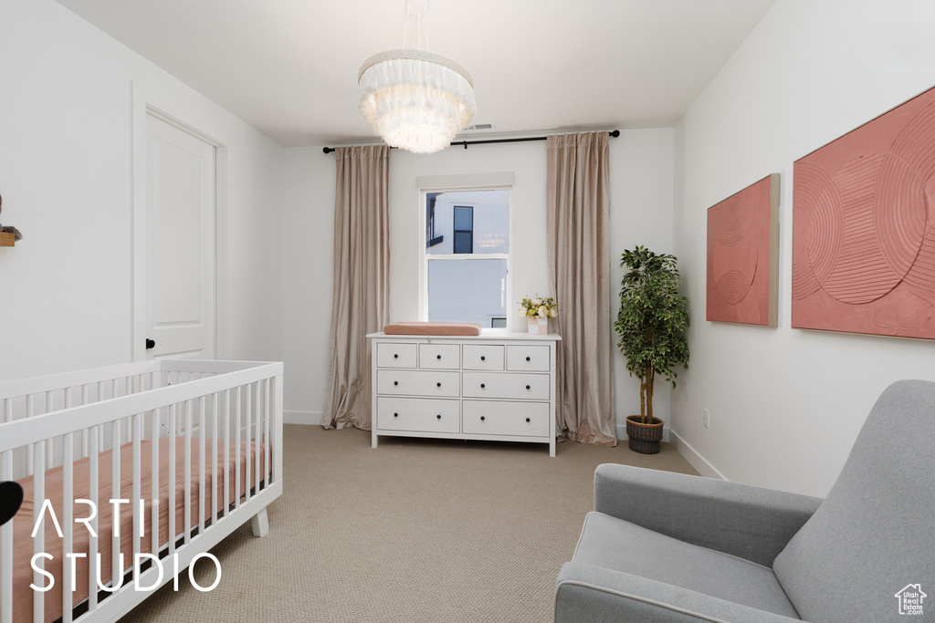 Carpeted bedroom with a crib, baseboards, and a chandelier