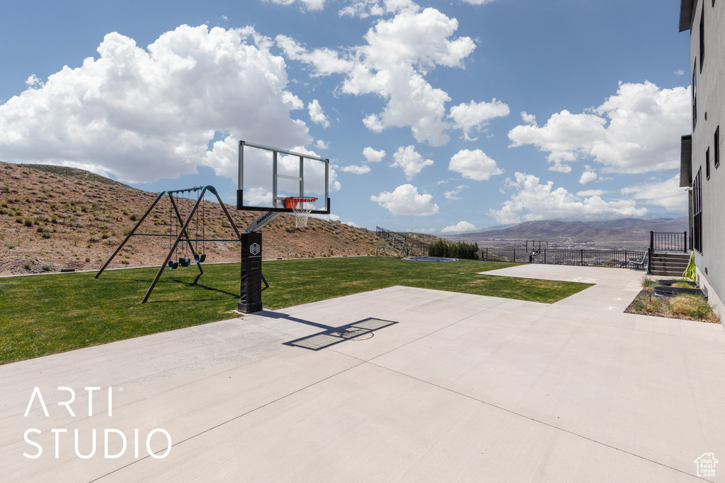 View of basketball court featuring basketball court, fence, a mountain view, a playground, and a yard