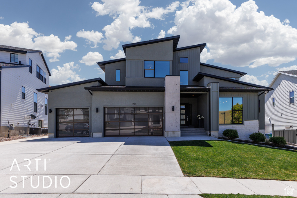 Contemporary home with an attached garage, a front lawn, fence, and driveway