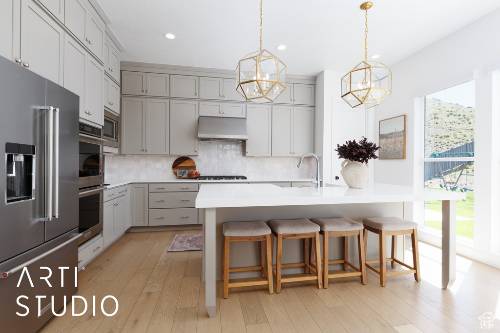 Kitchen with stainless steel appliances, gray cabinetry, a sink, a chandelier, and under cabinet range hood