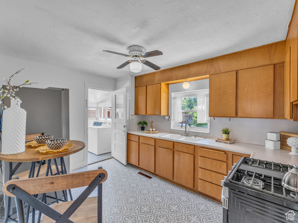 Kitchen with a sink, washer / dryer, light countertops, black range with gas cooktop, and ceiling fan