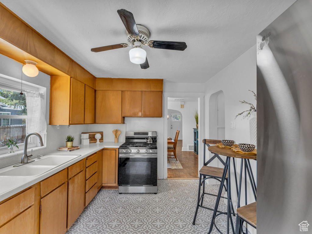 Kitchen featuring gas range, a sink, arched walkways, light countertops, and a ceiling fan