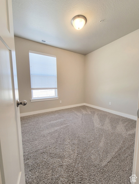 Empty room with a textured ceiling, carpet, baseboards, and visible vents