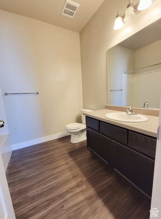 Full bath with toilet, wood finished floors, visible vents, walk in shower, and vanity
