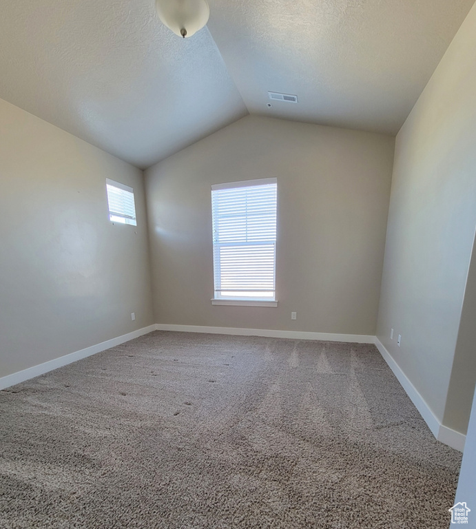 Carpeted spare room with a textured ceiling, vaulted ceiling, baseboards, and visible vents