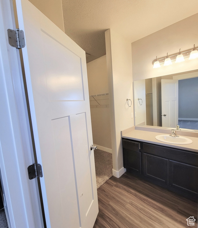 Bathroom featuring a textured ceiling, baseboards, vanity, a walk in closet, and wood finished floors
