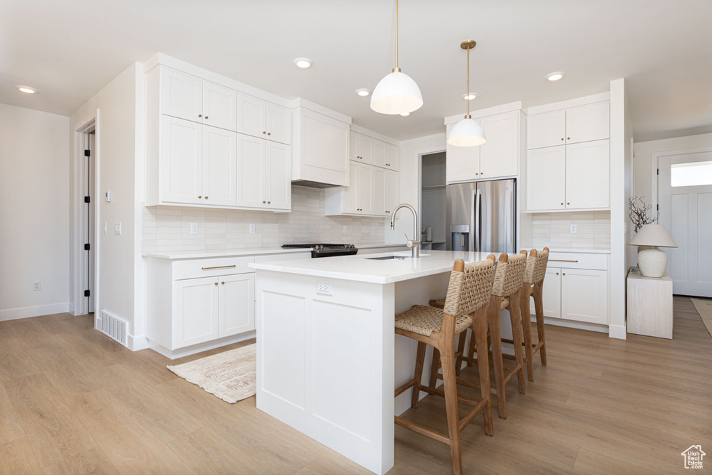 Kitchen with a sink, stainless steel fridge, tasteful backsplash, light wood-style floors, and light countertops