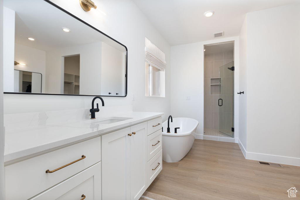 Bathroom featuring a shower stall, vanity, wood finished floors, a soaking tub, and baseboards