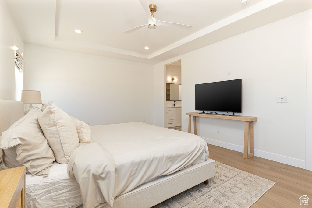 Bedroom featuring light wood-style flooring, baseboards, recessed lighting, a tray ceiling, and connected bathroom