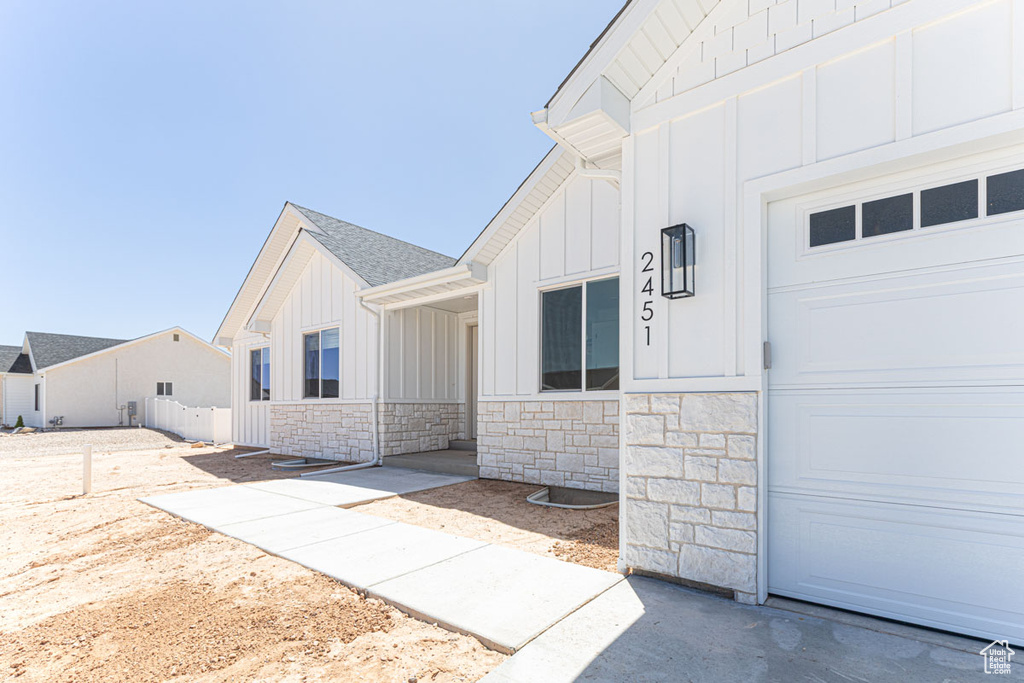 Entrance to property featuring board and batten siding, stone siding, a garage, and fence