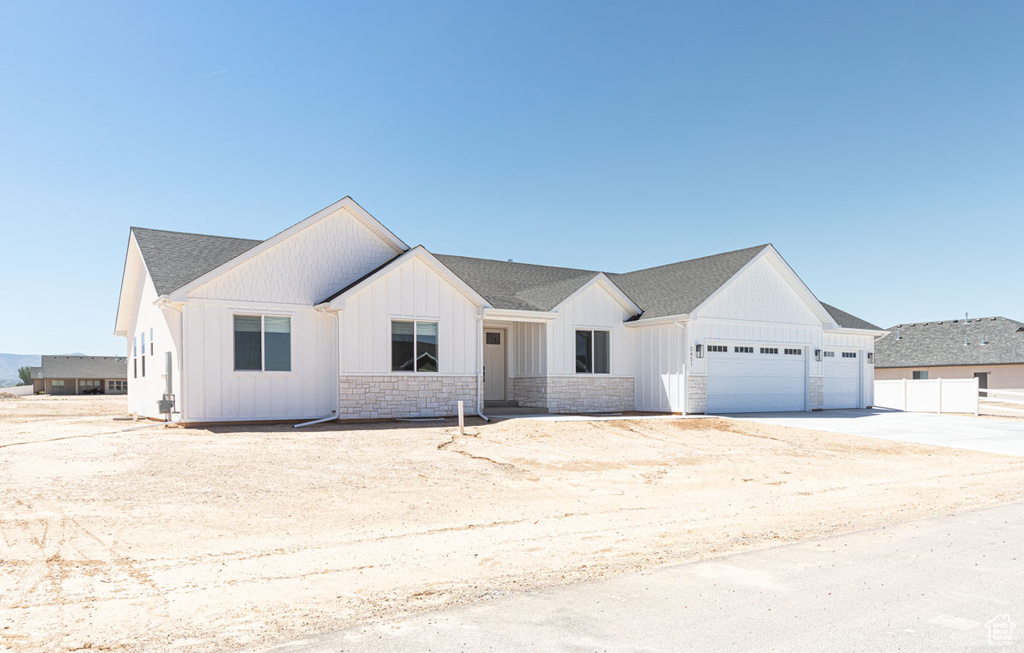 Modern farmhouse with a garage, board and batten siding, driveway, stone siding, and fence