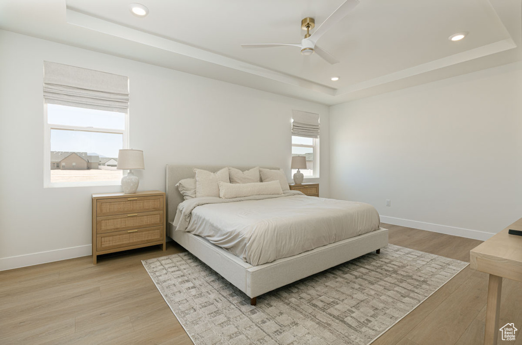 Bedroom featuring a tray ceiling, light wood-type flooring, baseboards, recessed lighting, and ceiling fan
