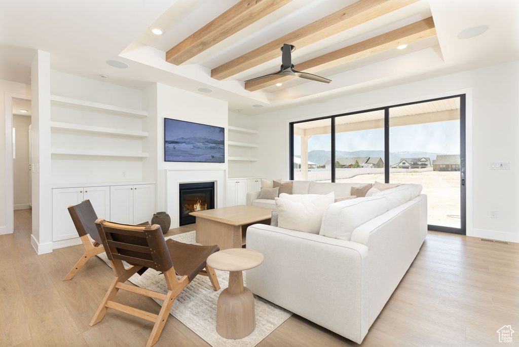 Living area featuring a glass covered fireplace, baseboards, built in features, light wood-style floors, and recessed lighting
