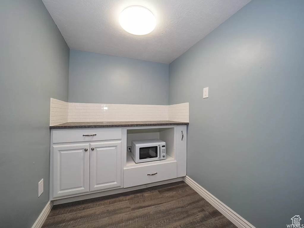 Kitchen featuring dark wood finished floors, tasteful backsplash, dark countertops, white cabinetry, and baseboards