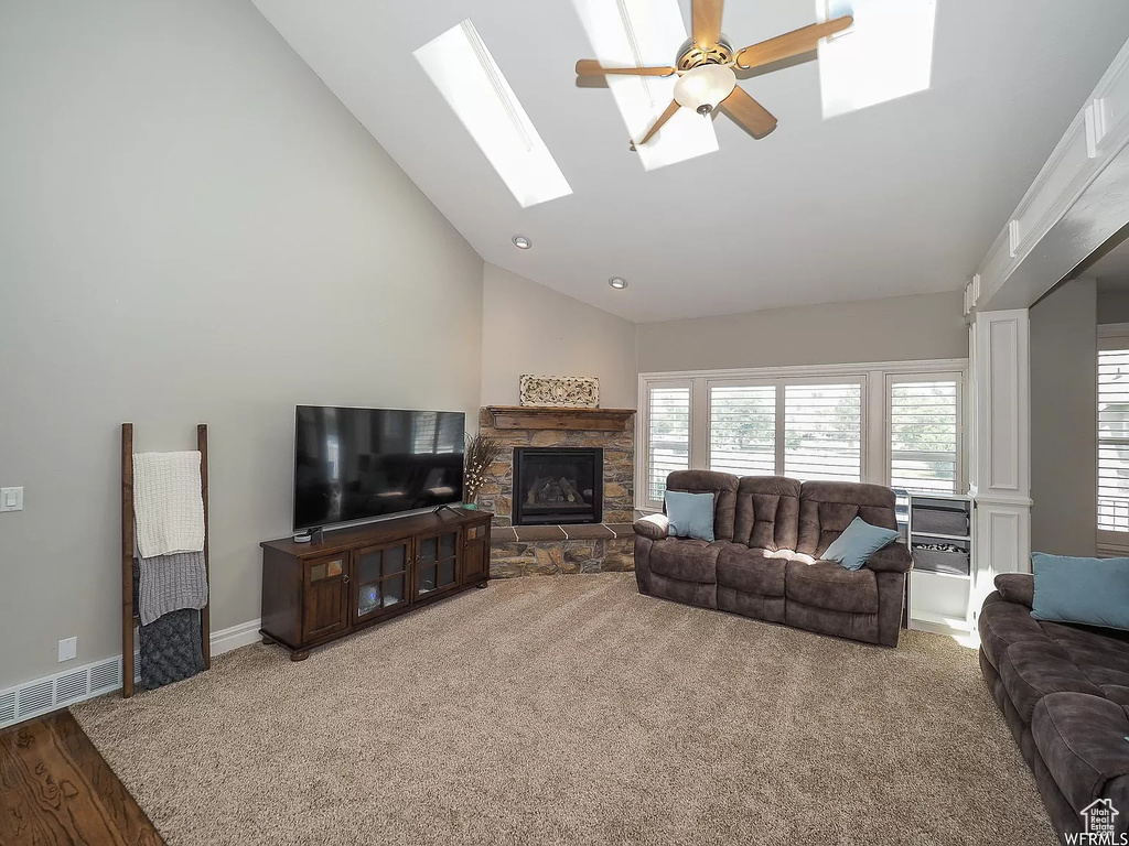 Living room featuring a skylight, a ceiling fan, a fireplace, high vaulted ceiling, and carpet flooring