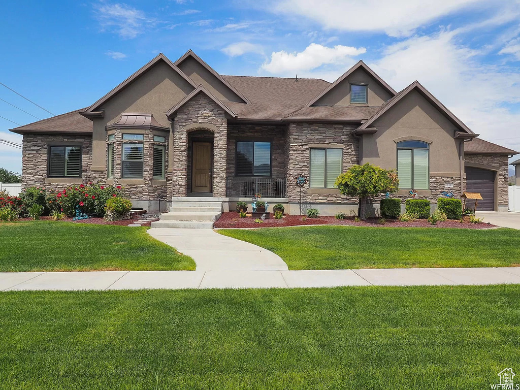 View of front facade featuring stone siding, stucco siding, a front yard, and roof with shingles