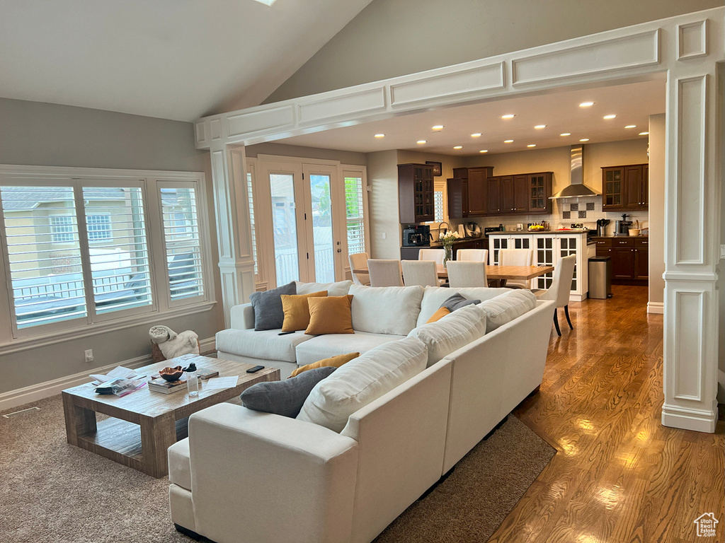 Living room with high vaulted ceiling, recessed lighting, wood finished floors, and ornate columns