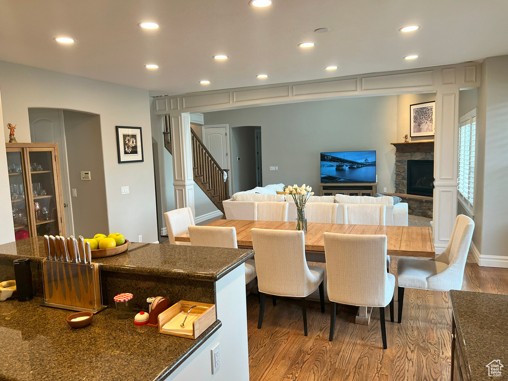 Dining area with wood finished floors, recessed lighting, a stone fireplace, and stairs