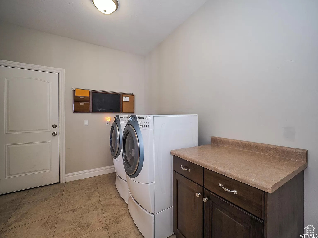 Clothes washing area with washing machine and dryer, baseboards, and cabinet space