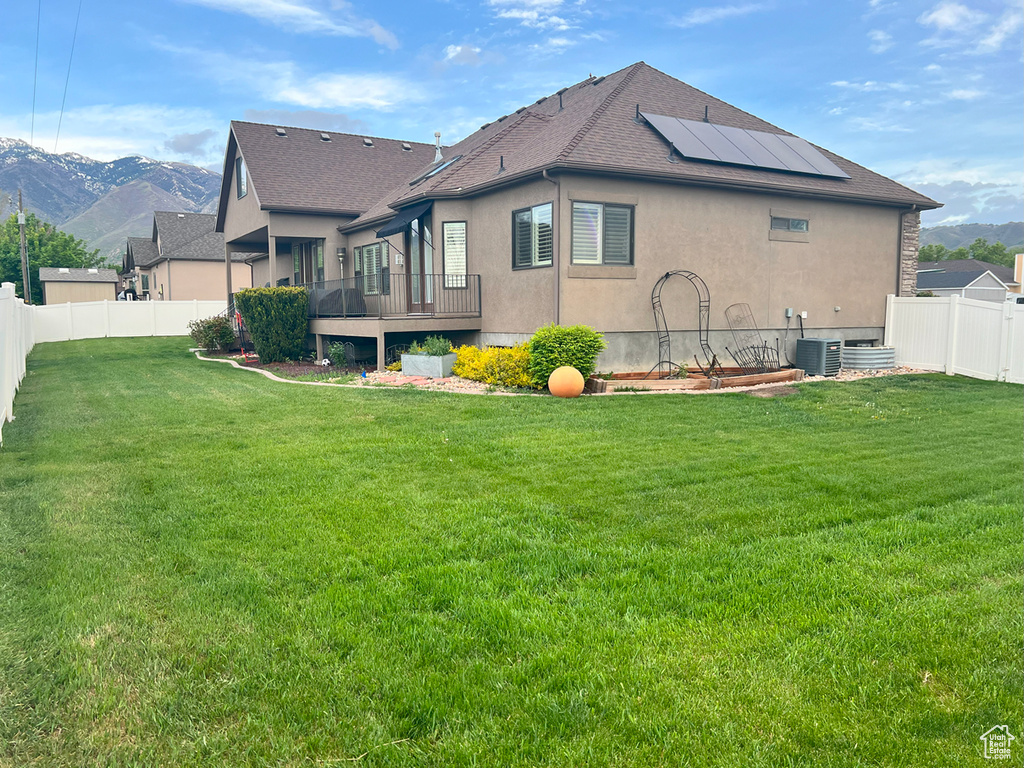 Rear view of house featuring stucco siding, roof mounted solar panels, roof with shingles, central AC, and a deck with mountain view