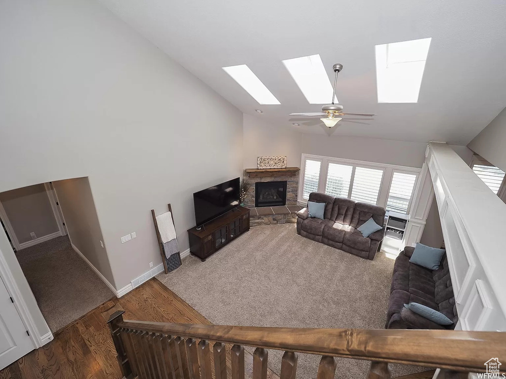 Living room featuring a skylight, a stone fireplace, a ceiling fan, wood finished floors, and high vaulted ceiling