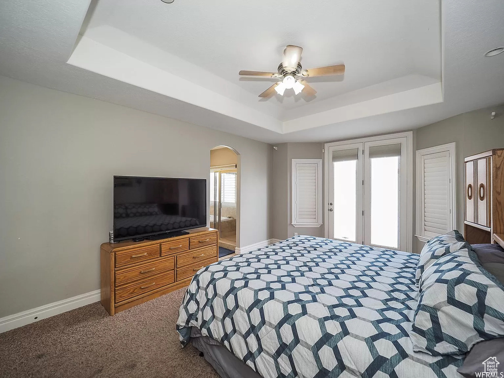 Carpeted bedroom with a tray ceiling, baseboards, arched walkways, and a ceiling fan