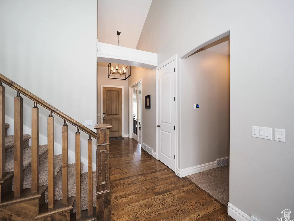 Corridor featuring dark wood-style floors, a chandelier, arched walkways, baseboards, and high vaulted ceiling