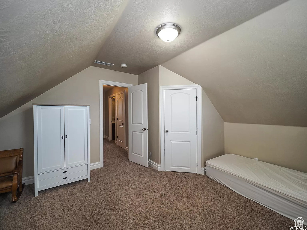 Unfurnished bedroom featuring carpet floors, vaulted ceiling, a textured ceiling, and baseboards