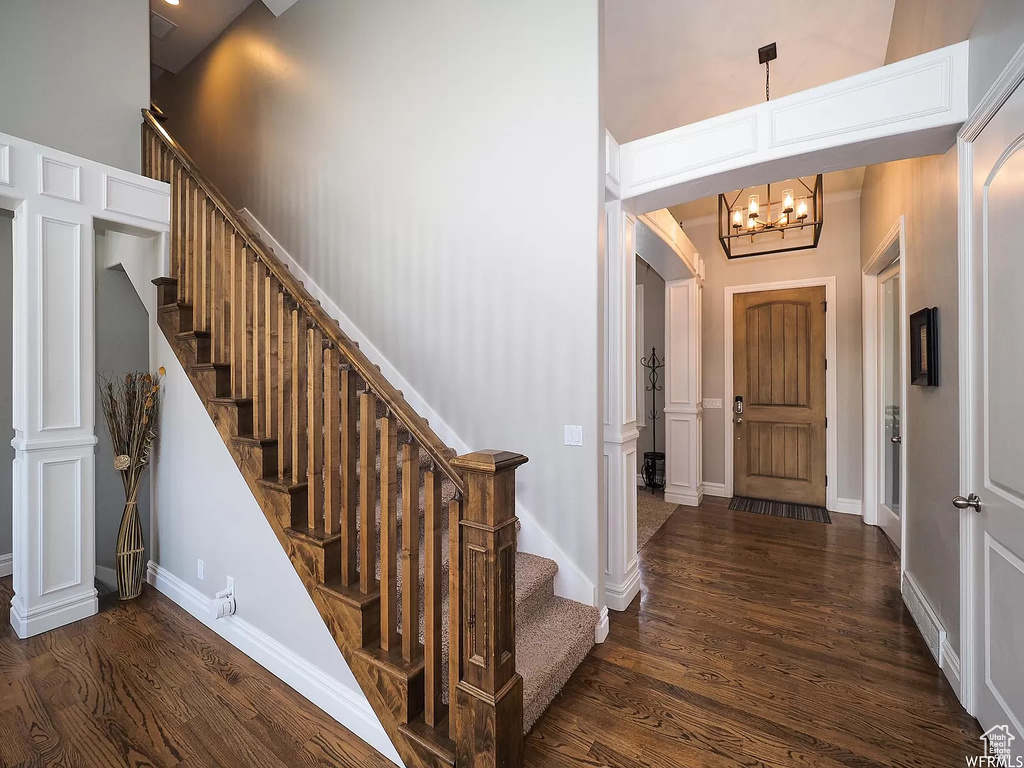 Entrance foyer featuring wood finished floors, a chandelier, a high ceiling, stairway, and baseboards
