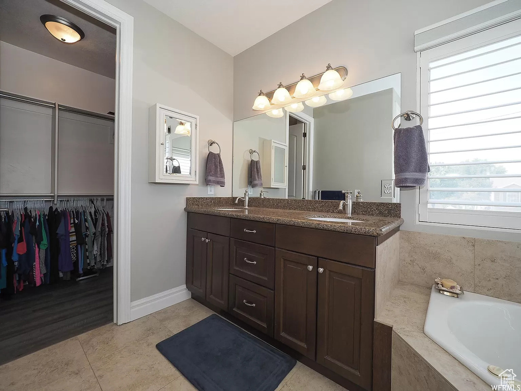 Bathroom with plenty of natural light, double vanity, baseboards, and tiled tub