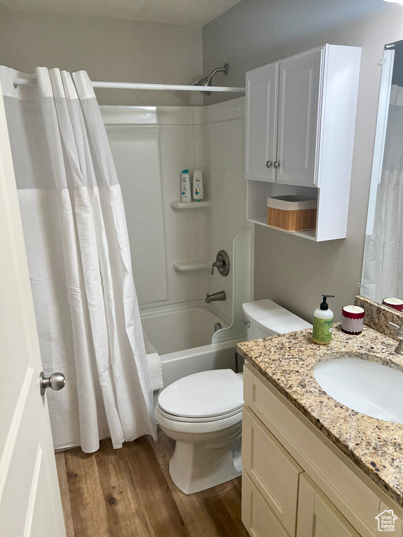 Bathroom featuring wood finished floors, toilet, shower / bath combo with shower curtain, and vanity