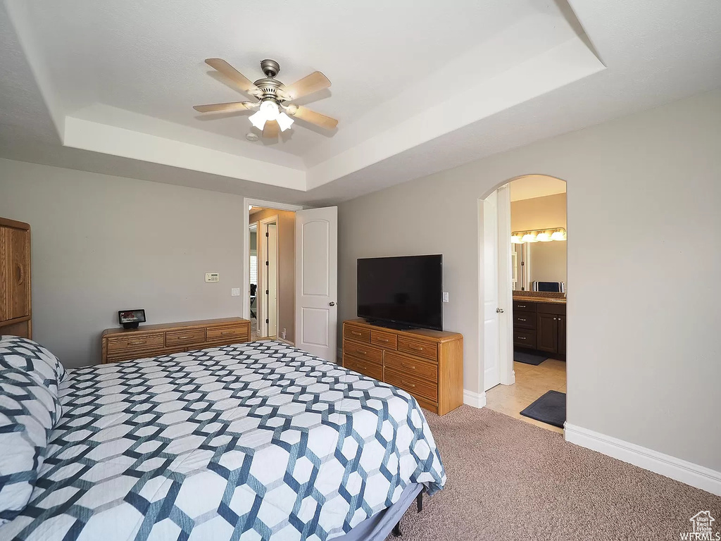 Bedroom featuring a raised ceiling, light colored carpet, arched walkways, baseboards, and a ceiling fan