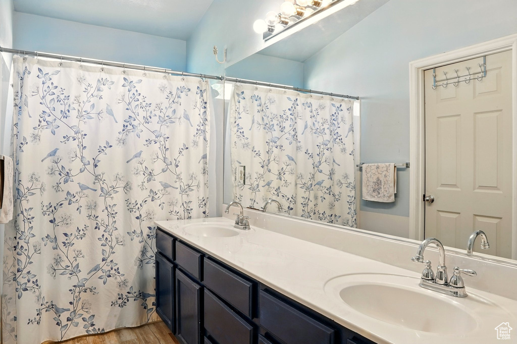 Full bath with double vanity, a shower with shower curtain, and wood finished floors