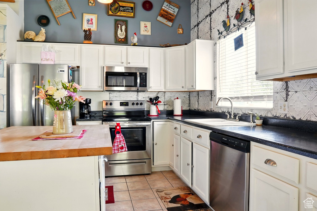 Kitchen with appliances with stainless steel finishes, a sink, light tile patterned floors, white cabinetry, and tasteful backsplash