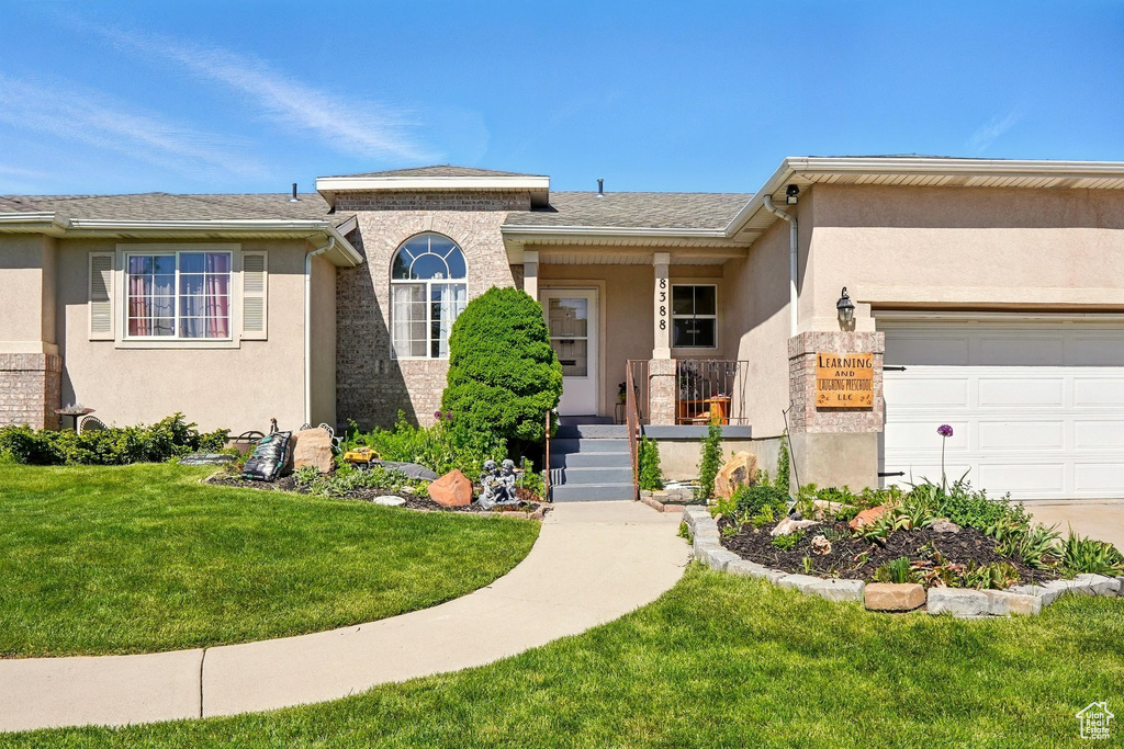 View of front of home featuring an attached garage, a front lawn, stucco siding, and covered porch