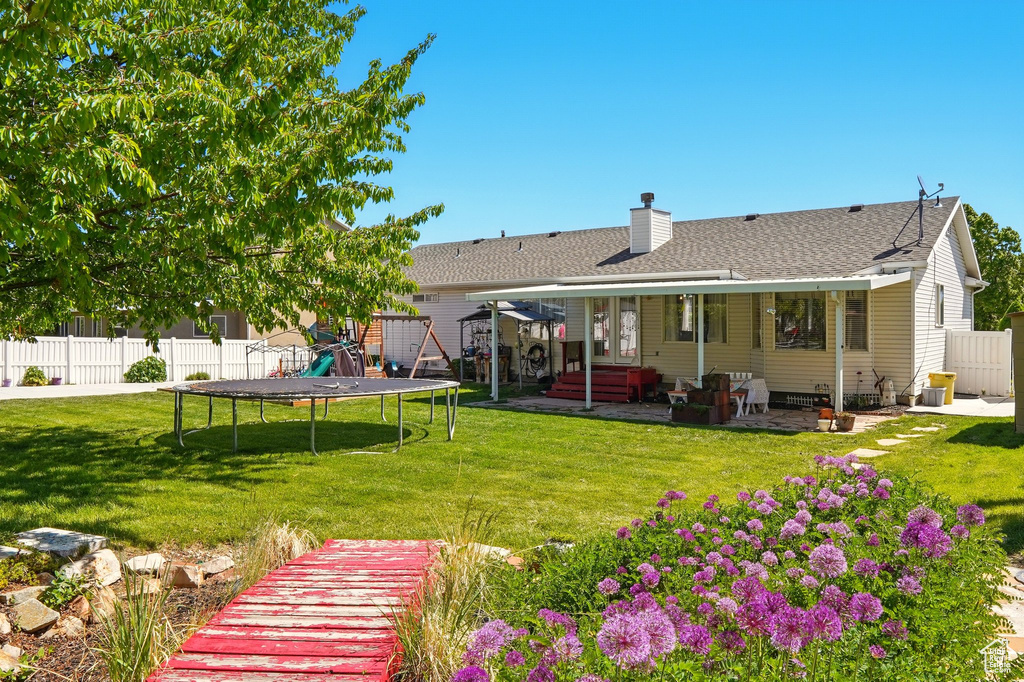Rear view of property with a trampoline, a chimney, a patio, and a shingled roof