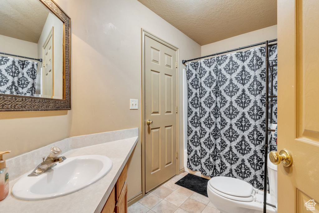 Full bath with a textured ceiling, vanity, toilet, tile patterned flooring, and curtained shower