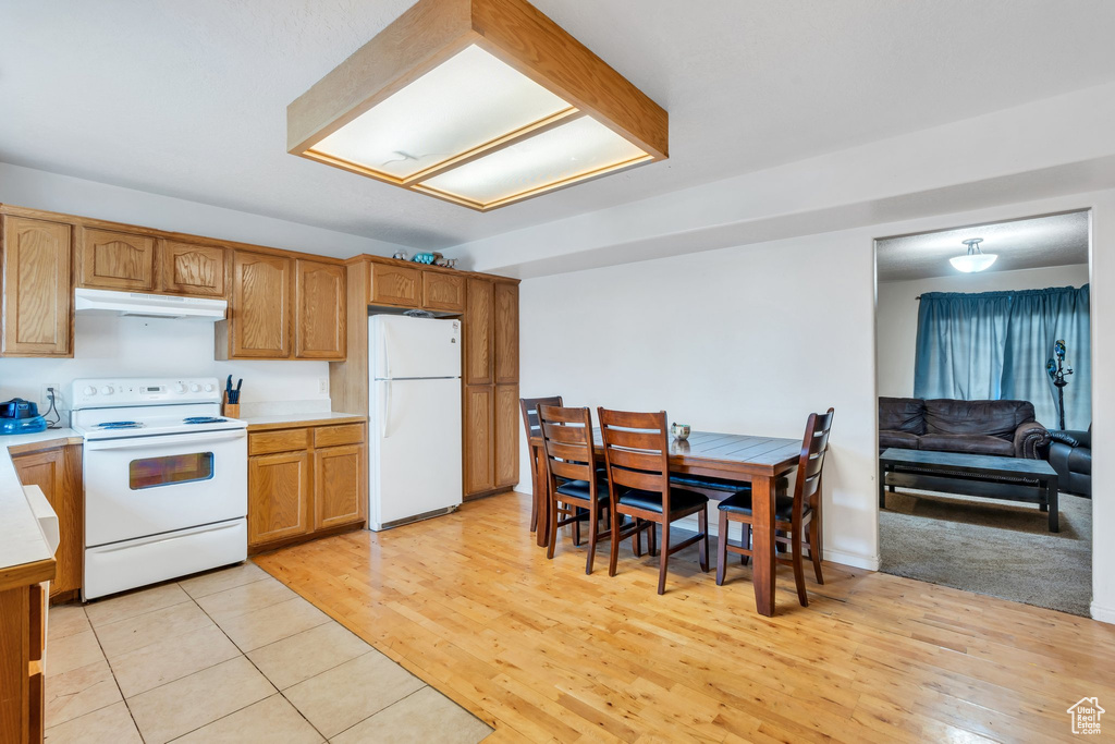 Kitchen featuring white appliances, under cabinet range hood, light countertops, light wood-type flooring, and brown cabinets