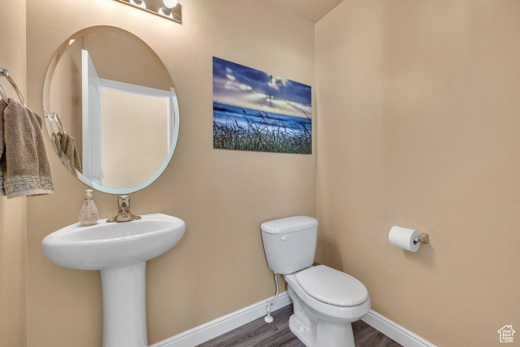 Bathroom featuring toilet, wood finished floors, baseboards, and a sink