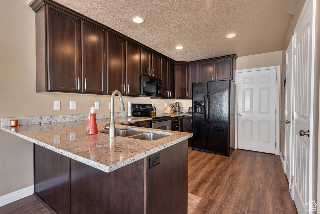 Kitchen featuring black appliances, a sink, dark brown cabinetry, a peninsula, and light stone countertops