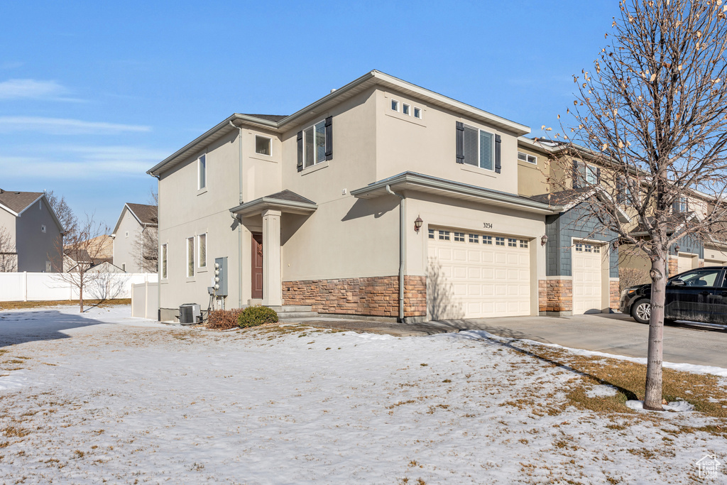 View of front of property featuring stone siding, fence, an attached garage, stucco siding, and driveway