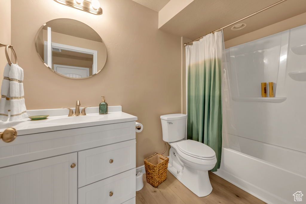 Full bathroom featuring toilet, wood finished floors, vanity, and shower / bathtub combination with curtain