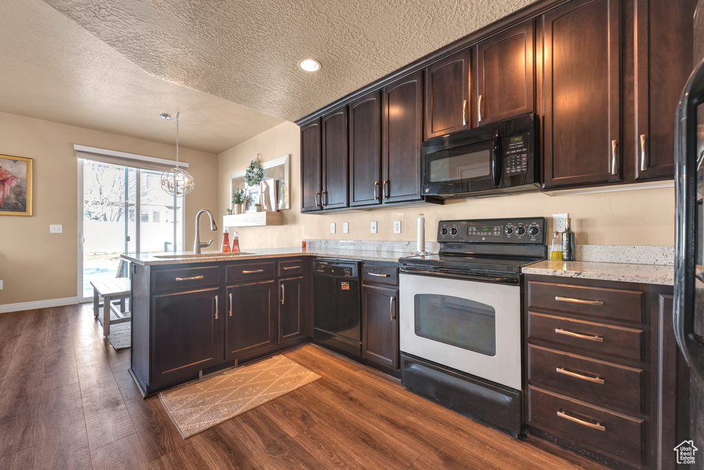 Kitchen with black appliances, a sink, a peninsula, dark wood-type flooring, and a textured ceiling