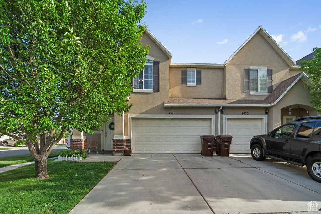 Townhome / multi-family property featuring an attached garage, driveway, stucco siding, a front lawn, and brick siding