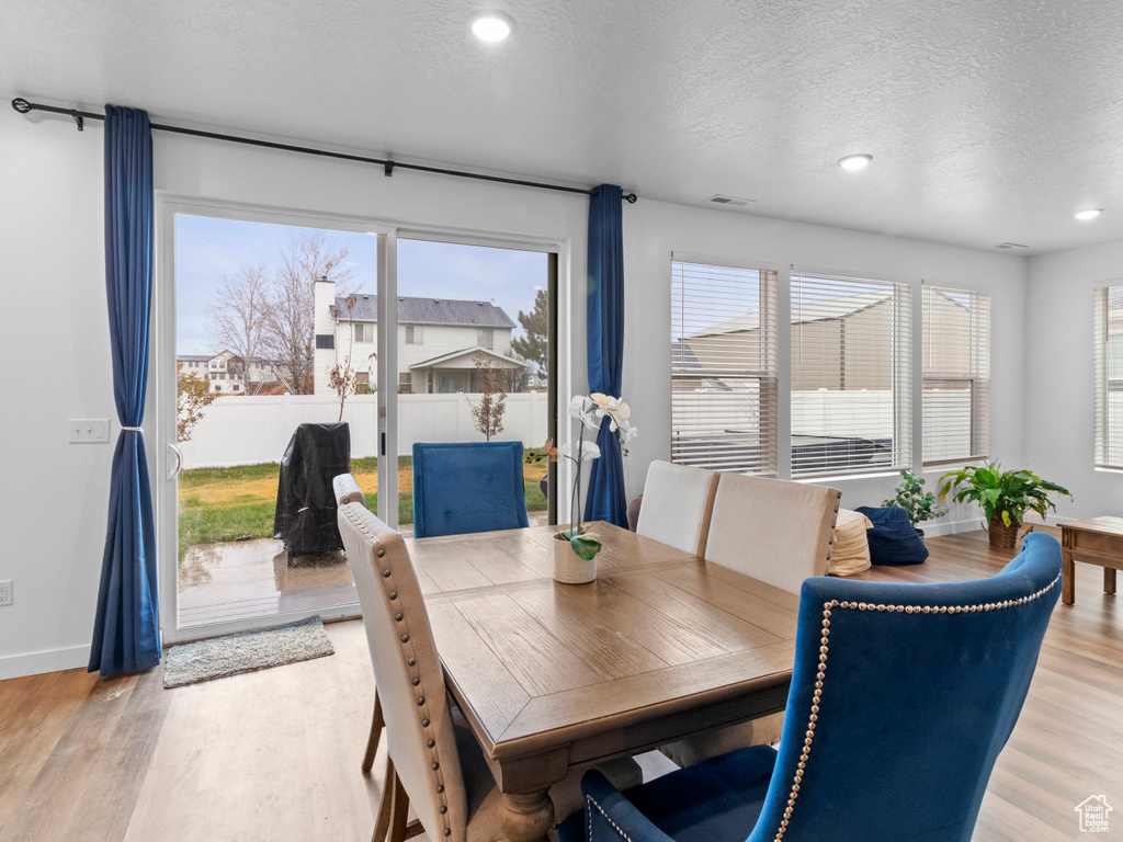 Dining room with a textured ceiling, light wood-type flooring, recessed lighting, and baseboards